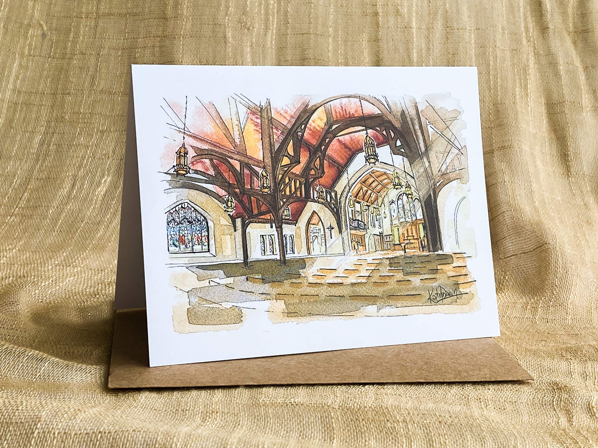 Watercolor sketch greeting card of Christ Church Cathedral interior, Vancouver, showing wooden vaulted arches, hanging lanterns, and stained glass windows, displayed with a kraft paper envelope.