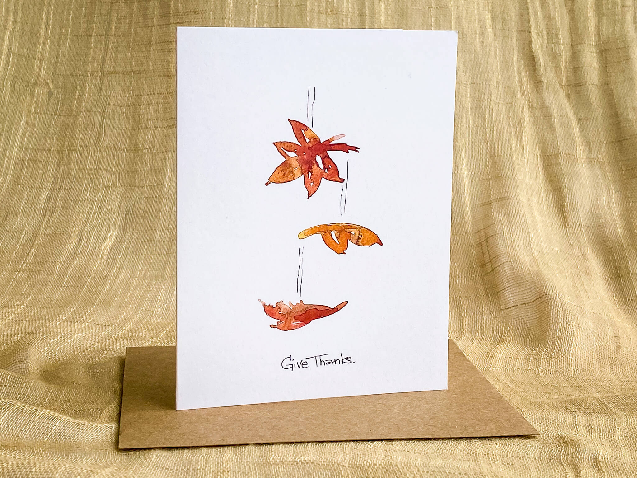 Thanksgiving greeting card featuring hand-painted watercolor autumn leaves and 'Give Thanks' script, paired with a kraft paper envelope.