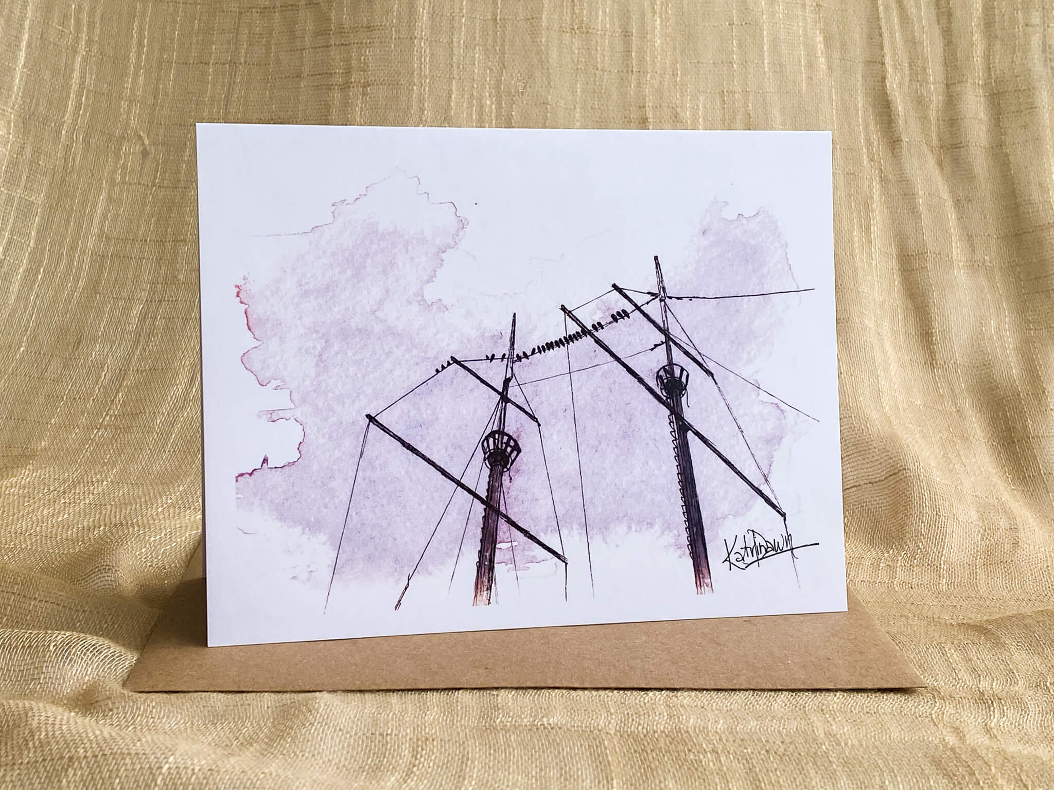 Watercolor and ink greeting card by Katrina Dawn featuring a close-up of tall ship masts and rigging silhouetted against a soft pink sky, shown with a kraft paper envelope.