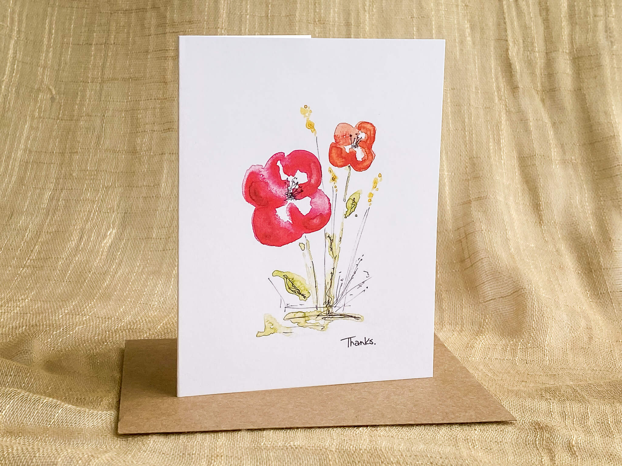 Watercolor thank you greeting card by Katrina Dawn featuring hand-painted red and orange flowers with 'Thanks' script, paired with a kraft paper envelope.